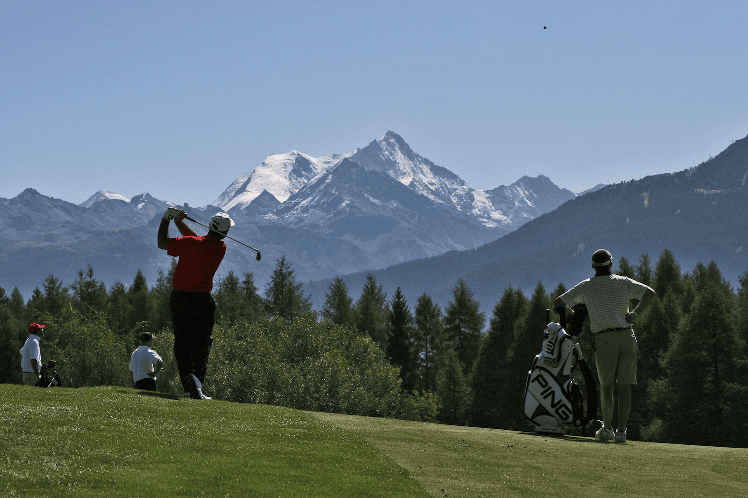 Golfurlaub Tirol – Golfspieler beim Abschlag auf einem alpinen Golfplatz mit Blick auf die majestätischen Tiroler Berge und schneebedeckten Gipfeln.